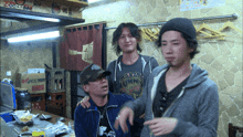 three men are standing in a room with a sign on the wall that says " coca-cola "