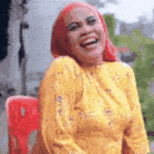 a woman wearing a yellow shirt and a red head scarf is laughing while sitting in a red chair .