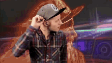 a man wearing a plaid shirt and a hat with the letter s on it adjusts his earbuds