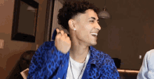 a young man wearing a blue leopard print jacket is smiling and laughing