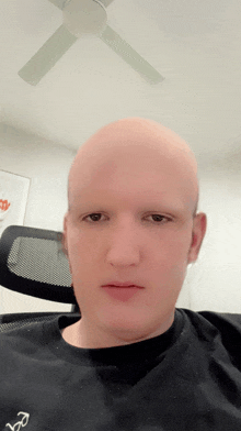a bald man wearing a black shirt with the letter r on the front