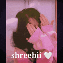 a girl in a pink sweater is covering her face with her hands and the name sreebii is on the bottom right