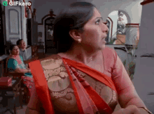 a woman in a red and gold saree is standing in front of a group of people in a living room .