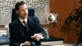 a man in a suit and tie is sitting at a desk using a calculator and a mouse .