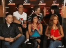 a group of people are sitting in a dark room with a man wearing a striped shirt .