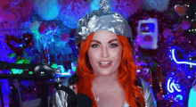 a woman with red hair is wearing a tin foil hat and standing in front of a microphone .