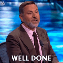 a man in a suit and tie is sitting in front of a microphone and says well done .