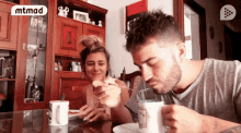a man and a woman are sitting at a table eating food with a mtmad logo in the background