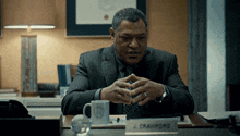 a man in a suit sits at a desk with a name plate that says j. crawford