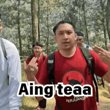a man wearing a red shirt that says " aing teaa " is giving the middle finger