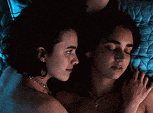 two women are laying on a bed and one has a necklace on her neck