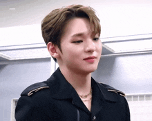 a young man wearing a black jacket and a gold necklace