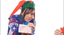 a woman wearing an elf hat and sweater is holding a christmas stocking