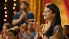 a woman is clapping her hands in a crowd of people .