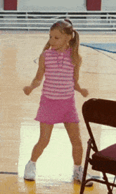 a little girl in a pink skirt and striped shirt is dancing on a basketball court