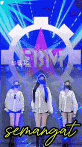 three women wearing face masks stand in front of a sign that says semangat