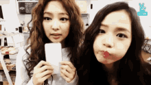 two young women are making funny faces while holding a cell phone .
