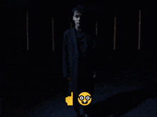 a man in a black coat is standing in the dark with a yellow smiley face and a finger pointing up