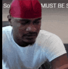 a man wearing a red hat and a white shirt is sitting in front of a sign that says so must be so