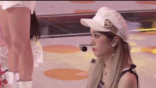 a woman wearing a hat and a microphone is sitting on the floor .