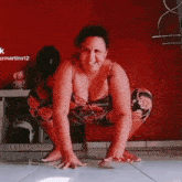 a woman is squatting on the floor in front of a red wall and smiling .