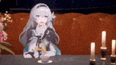 a girl is sitting at a table with candles and a cup of tea .