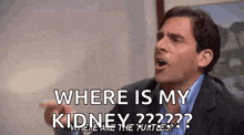 a man in a suit and blue shirt is pointing at something and asking where is my kidney ?