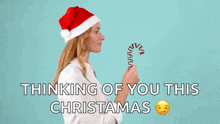 a woman wearing a santa hat is holding a candy cane with the words " thinking of you this christmas " below her
