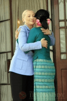 a woman in a blue jacket is hugging a woman in a green skirt