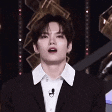 a young man in a suit and white shirt is standing on a stage with a microphone .