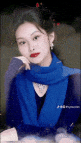 a woman wearing a blue scarf and a necklace is looking at the camera