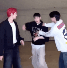 three young men are standing next to each other in a room and one of them is wearing a shirt that says kith .