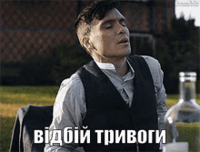 a man in a suit and vest is sitting next to a bottle of alcohol and a foreign language written on the image