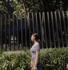 a woman in a blue off the shoulder top stands in front of a fence