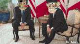 two men in suits are sitting on a couch and one of them has a monkey face on his head