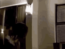 a person is standing in a room next to a window with blinds on it .