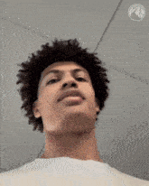 a young man with curly hair looks at the camera with a basketball logo in the background