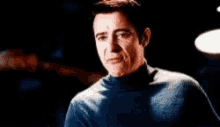 a man in a blue turtleneck is making a funny face in a dark room .