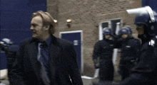 a man in a suit and tie stands in front of a group of police
