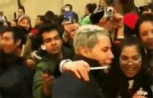 a man with green hair is brushing his teeth in a crowd of people