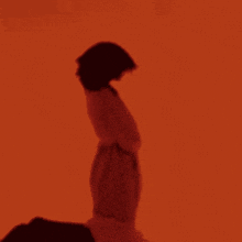 a woman in a red dress is standing in front of an orange wall