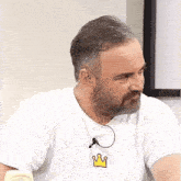 a man with a beard is wearing a white shirt with a yellow crown on the front