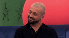 a man with a beard is smiling in front of a red , green and blue flag .