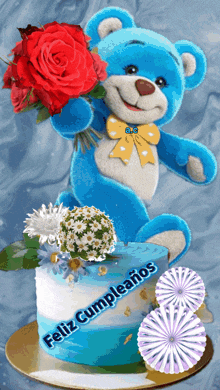 a blue teddy bear holding a bouquet of red roses next to a cake that says feliz cumpleaños