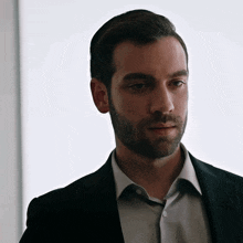 a man with a beard is wearing a black suit and white shirt