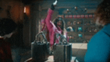 a woman in a pink jacket is standing in front of a table with a bunch of handbags .