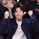 a young man in a blue jacket is making a funny face while holding his fist in the air .