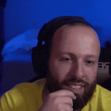 a bald man with a beard wears headphones and a yellow shirt