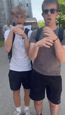 two young men are standing next to each other on a sidewalk . one of the men is wearing sunglasses .