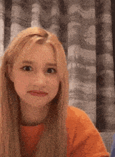 a woman with blonde hair is making a funny face while wearing an orange sweater .